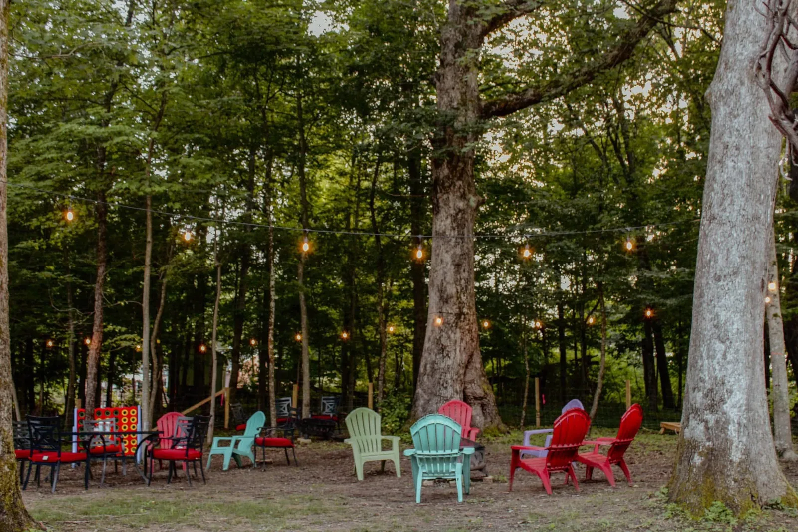 An outdoor firepit with chairs around it and lights hanging from the trees.
